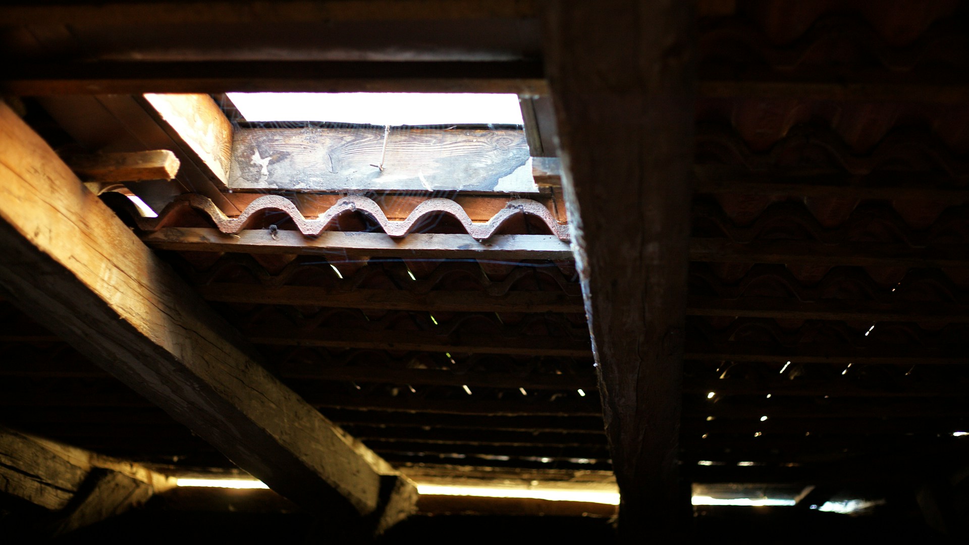 Foto da parte interna de um telhado, detalhando vigas de madeira e telhas