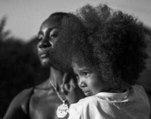 Foto em preto e branco de uma mulher negra com uma criança no colo