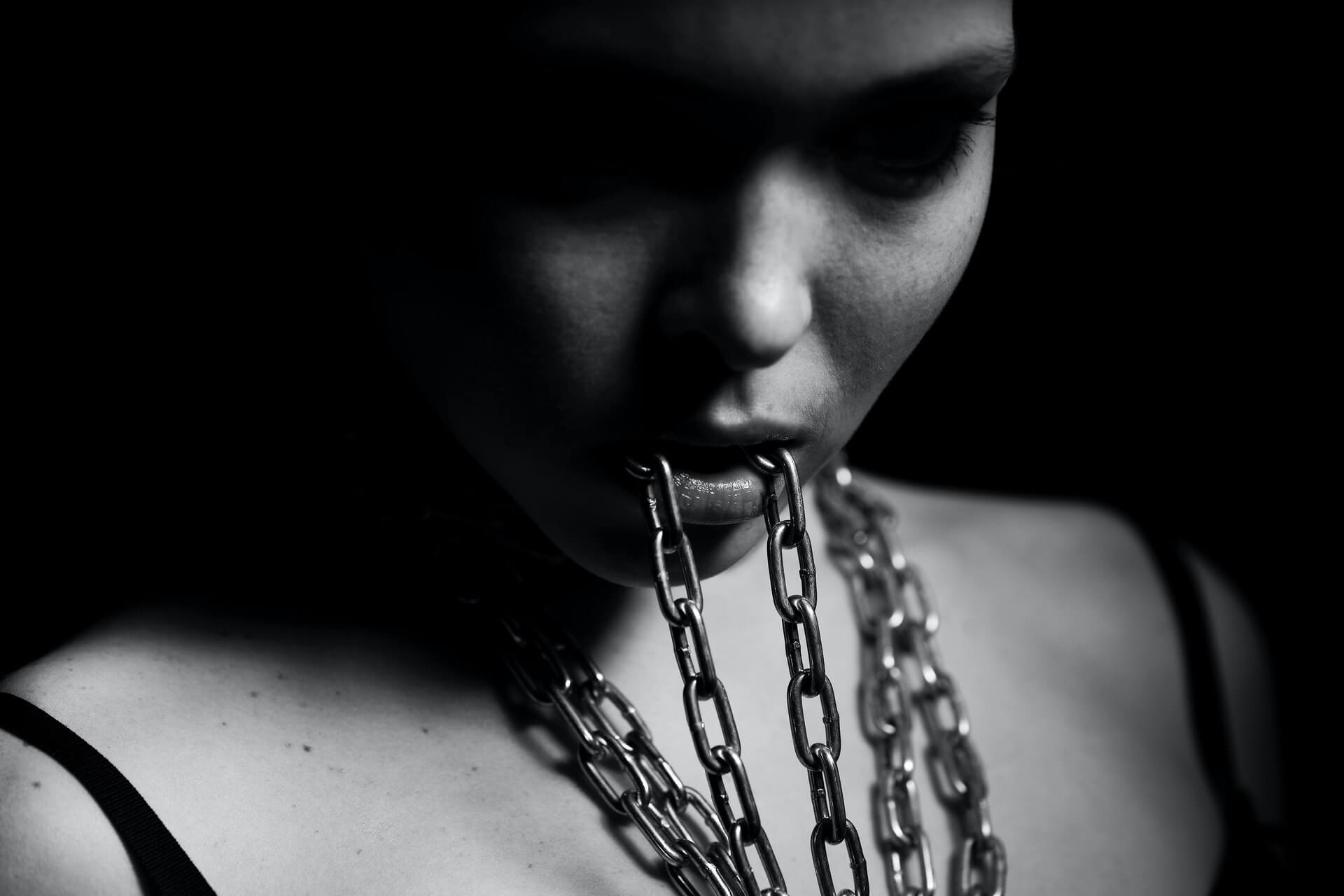 Foto aproximada em tons de cinza de uma mulher segurando uma corrente entre os dentes e em volta do pescoço