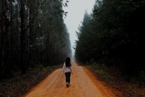 Foto de uma mulher caminhando por uma estrada de terra cercada de árvores abundantes em ambos os lados