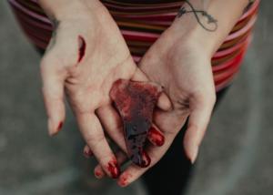 Foto detalhada das mãos de uma pessoa segurando um fragmento de vidro ensanguentado