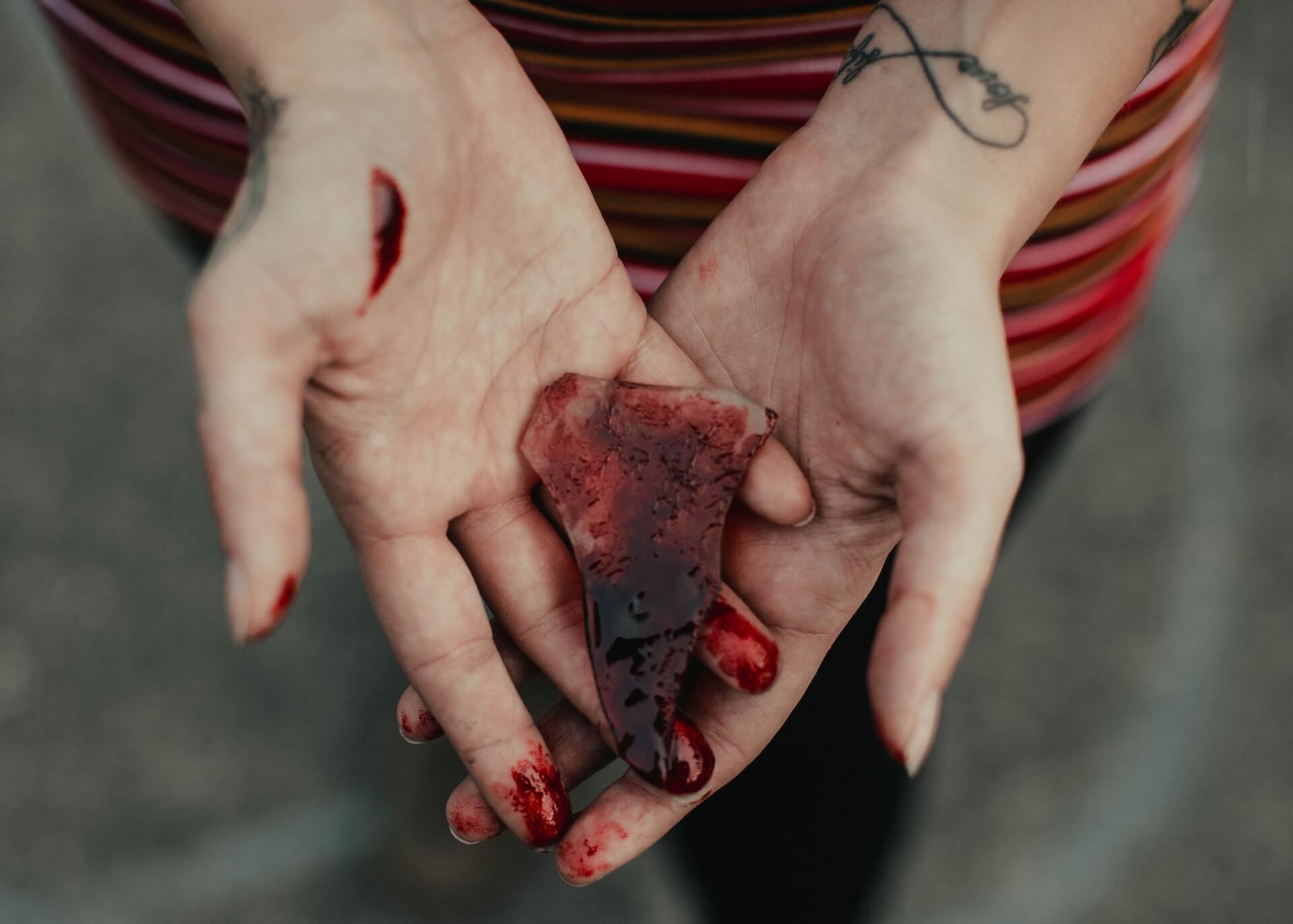 Foto detalhada das mãos de uma pessoa segurando um fragmento de vidro ensanguentado